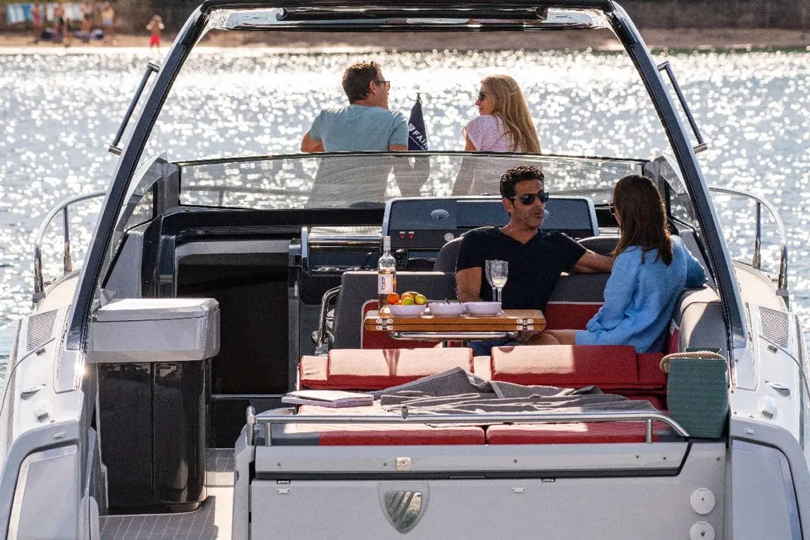 A couple sits on a yacht enjoying drinks and snacks, while two people chat in the background by the sparkling water.